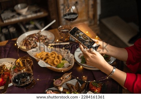 Young woman takes a photo of her food with a phone at a festive table