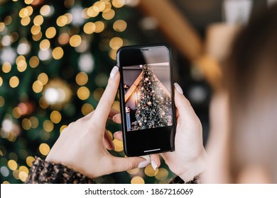 Young woman takes pictures of Christmas tree on smartphone. Close-up - Powered by Shutterstock