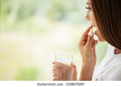 Young woman takes round pill with glass of water in hand - Shutterstock ID 2238070287