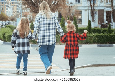 young woman takes two girls across the road in the city. Mom holds her daughters hands and teaches them to cross the road safely at a pedestrian crossing
