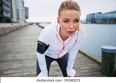 Young woman taking a break from exercise outdoors. Fit young female athlete stopping for rest while jogging along the river. - Powered by Shutterstock