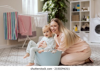 Young Woman Taking Care Of Sweet Blonde Daughter, Little Girl Helps Woman Sort Clothes For Laundry, Baby Sits In Bowl, Mom Hugs Baby.