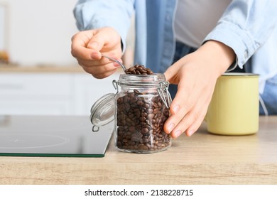 Young woman taking coffee beans from jar on counter in kitchen, closeup
