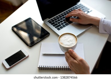 Young Woman Taking A Coffee Break As She Sits At A Table Working On A Laptop Computer, Tablet, Phone, Close Up Of Her Hands And The Drink. Desing In White Color. Buisness Background