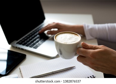 Young Woman Taking A Coffee Break As She Sits At A Table Working On A Laptop Computer, Tablet, Phone, Close Up Of Her Hands And The Drink. Desing In White Color. Buisness Background