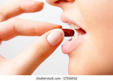 Young Woman Taking Dark Red Pill. Closeup.