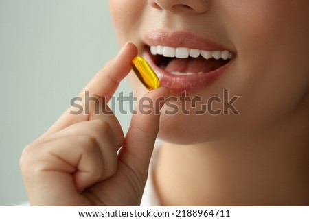 Young woman taking dietary supplement pill on blurred background, closeup