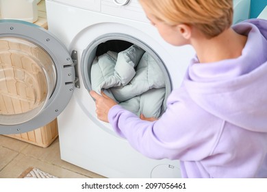 Young woman taking down jacket from washing machine in bathroom