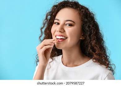 Young Woman Taking Fish Oil Pill On Color Background