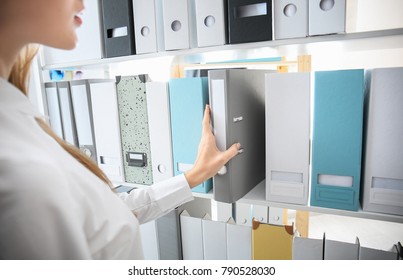 Young woman taking folder with documents from shelf in archive
