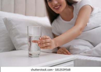 Young woman taking glass of water from nightstand at home, closeup