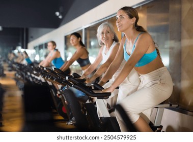 Young woman taking indoor cycling class at fitness center, doing cardio riding bike - Powered by Shutterstock