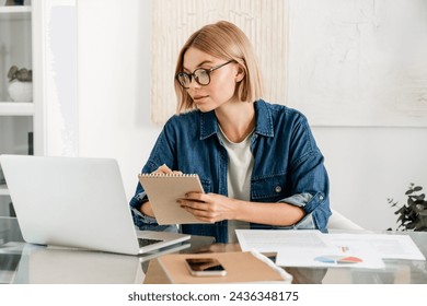 Young woman taking notes using laptop for remote studies at home desk. Smart freelancer watching learning educational webinar, counting charts and finances - Powered by Shutterstock