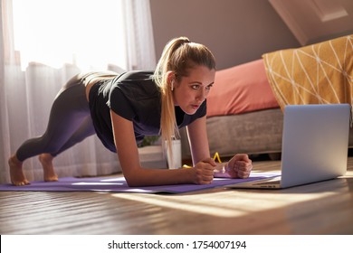 Young Woman Taking Part In Online Fitness Class In Front Of Laptop.