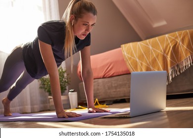 Young Woman Taking Part In Online Fitness Class In Front Of Laptop.