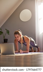 Young Woman Taking Part In Online Fitness Class In Front Of Laptop.