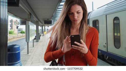 Young Woman Taking Phone Out Of Purse To Send Text While At Train Station