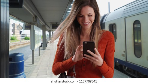 Young Woman Taking Phone Out Of Purse To Send Text While At Train Station