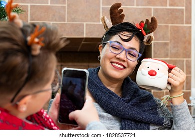 A young woman taking a photo of her girlfriend with a christmas cup in front of the christmas tree - Shutterstock ID 1828537721