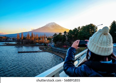 Young Woman taking photo with her phone of the view Mt.Fuji with Beautiful sunset at Lake Kawaguchiko in winter , Japan