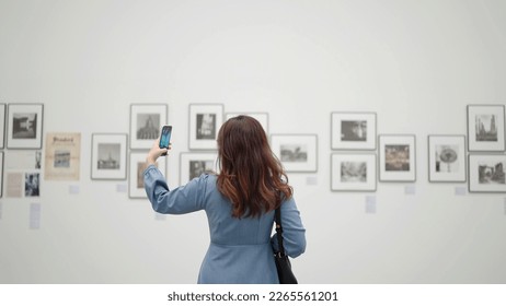 A young woman is taking photo of painting using camera of smartphone is photographing picture in gallery - Powered by Shutterstock