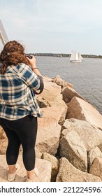 A Young Woman Taking A Photo Of A Passing Sailboat