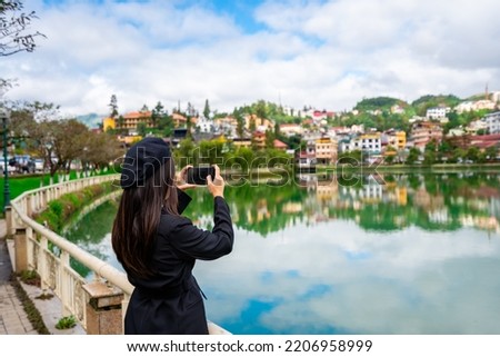 Young woman taking a photo at Sapa lake with reflection and blue sky in Lao Cai province, Vietnam