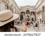 Young woman taking a photograph in a busy city square with people walking around in Split, Croatia