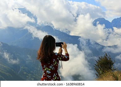 Young woman taking a picture of a beautiful cloudy mountain landscape  