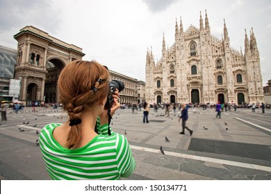 Young woman taking picture of Duomo di Milano (Milan Cathedral), Milan, Italy, motion blurred people on square