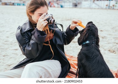 Young Woman Taking Picture Of Her Dog With Vintage Film Camera While Playing On The Beach