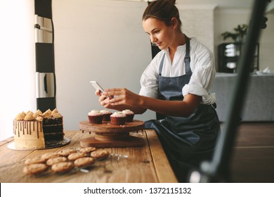 Young woman taking pictures of a cake in the kitchen. Female baker capturing photos of pastry items with her mobile phone. - Powered by Shutterstock