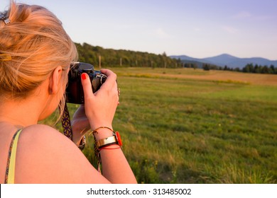 Young woman taking pictures at sunset with a digital camera in Lake Placid area, Adirondack,  Upstate New York.  Photography, adventure, travel vacation, outdoors and life style concept