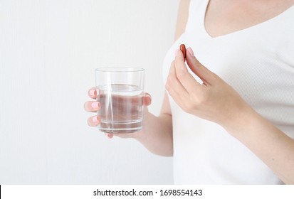 Young Woman Is Taking A Pill With A Glass Of Water On White Background With Copy Space