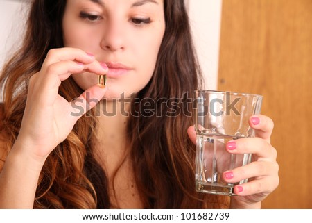A young woman taking a pill with a glass of water.