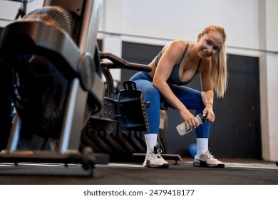 Young woman taking a rest on a rowing machine in a cross fit gym, catching her breath during an intense workout session. - Powered by Shutterstock