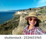 A young woman taking selfie near a cliffside view overlooking Okanagan lake. Kettle valley rail trail Penticton British Columbia, Canada. 