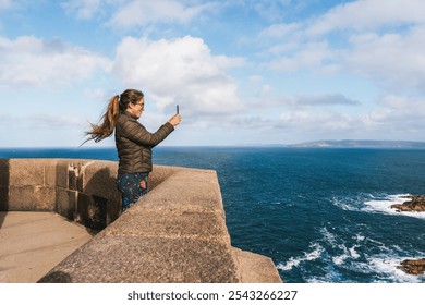 Young woman taking a selfie on a coastal lookout with panoramic ocean views at the tower of hercules - Powered by Shutterstock