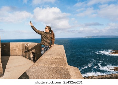 Young woman taking a selfie on a coastal lookout with panoramic ocean views at the tower of hercules - Powered by Shutterstock