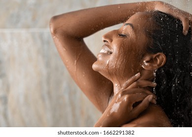 Young Woman Taking Shower Relaxing Under Warm Running Water. Smiling Beautiful Black Woman Enjoy During Hot Water Bath. Happy Girl With Closed Eyes In Shower Rinse Shampoo With Water Dripping On Face.