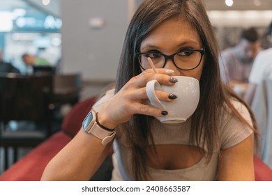 Young woman taking a sip of her delicious coffee. Close up image of a girl tasting her freshly brewed coffee while waiting for her next flight at an airport coffee shop. - Powered by Shutterstock