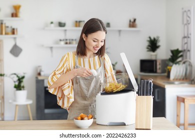 Young woman taking tasty french fries from deep fryer in kitchen