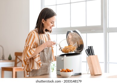 Young Woman Taking Tasty French Fries From Deep Fryer In Kitchen