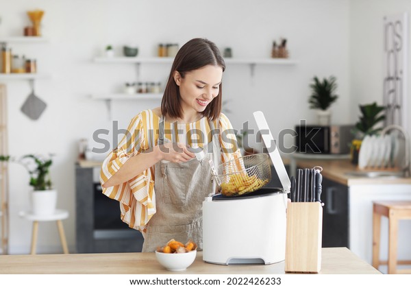 Young woman taking tasty french fries from deep\
fryer in kitchen