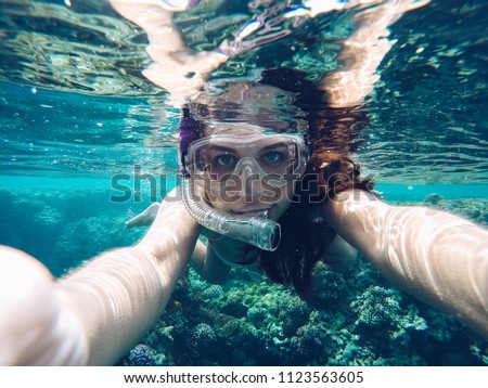 Young woman taking an underwater selfie wearing snorkeling mask when swiming and diving in red sea with clear turquoise blue water. Coral reef