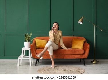 Young woman talking by mobile phone on red sofa near green wall - Powered by Shutterstock