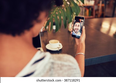 Young An And Woman Talking To Each Other Through A Video Call On A Smartphone. Young Woman Having A Videochat With Man On Mobile Phone. Woman Sitting At A Coffee Shop.