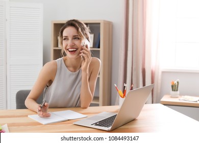 Young Woman Talking On Mobile Phone While Working With Laptop At Desk. Home Office