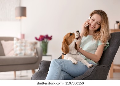 Young woman talking on phone while stroking her dog at home - Powered by Shutterstock