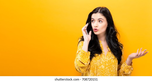 Young Woman Talking On The Phone On A Yellow Background